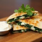 Finished Spinach and Feta Quesadilla with fresh cilantro and sour cream, ready to serve.