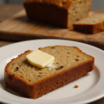 Freshly baked high altitude banana bread slice with butter on a cutting board.