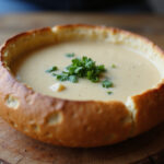 Finished sourdough bread bowl filled with soup and herbs, ready to serve.