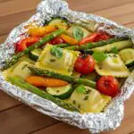 A deliciously plated foil-pack ravioli dinner featuring cheese-topped ravioli with vibrant vegetables, ready to enjoy.
