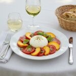 A beautifully styled dining setting with Peach Tomato Burrata Salad, wine, and bread, perfect for a summer meal.
