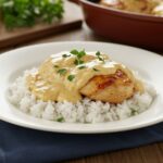Completed smothered chicken and rice dish, creamy and flavorful, garnished and ready to enjoy, the final presentation in a homey kitchen setting.
